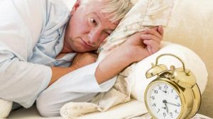 Sleepy elderly man waking up and looking at the alarm clock with one eye - focus is on the alarm clock